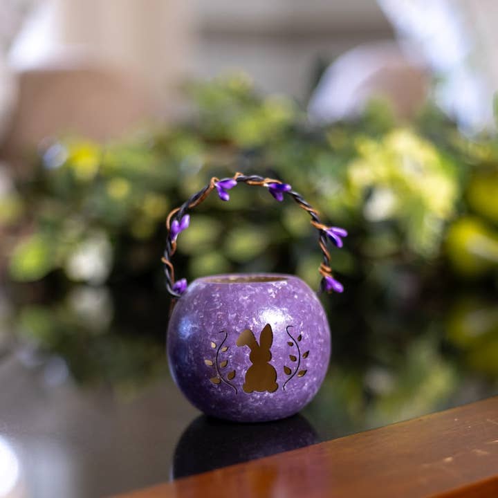 Purple decorative lantern with rabbit design on a reflective surface, blurred greenery in the background