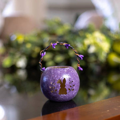 Purple decorative lantern with rabbit design on a reflective surface, blurred greenery in the background