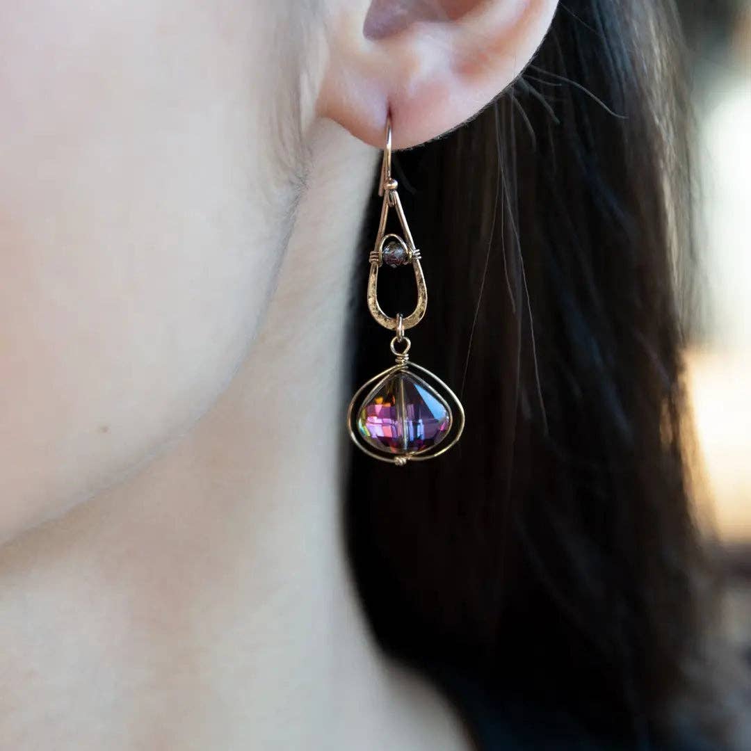 Close-up of a person wearing a decorative earring with a purple gemstone.