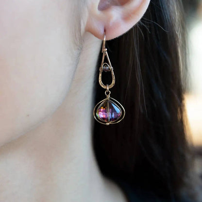 Close-up of a person wearing a decorative earring with a purple gemstone.