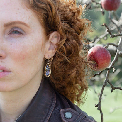 Close-up of a person with curly hair wearing earrings, with apples in the background.
