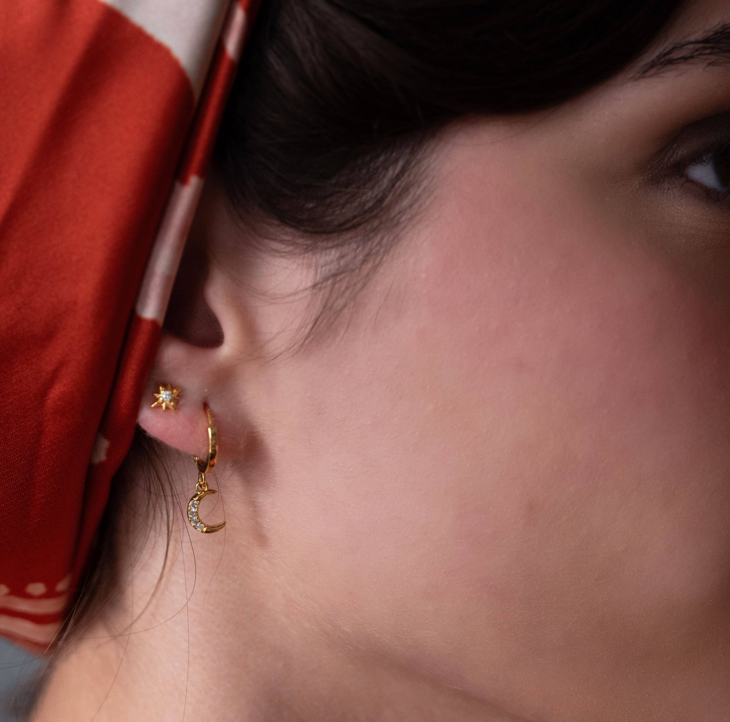 Close-up of a person wearing gold hoop earrings with a red head scarf