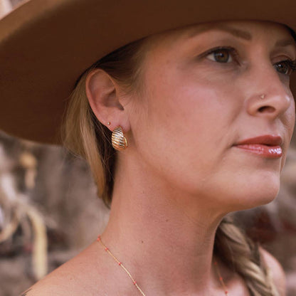 Woman wearing a wide-brimmed hat with gold earrings and a necklace.
