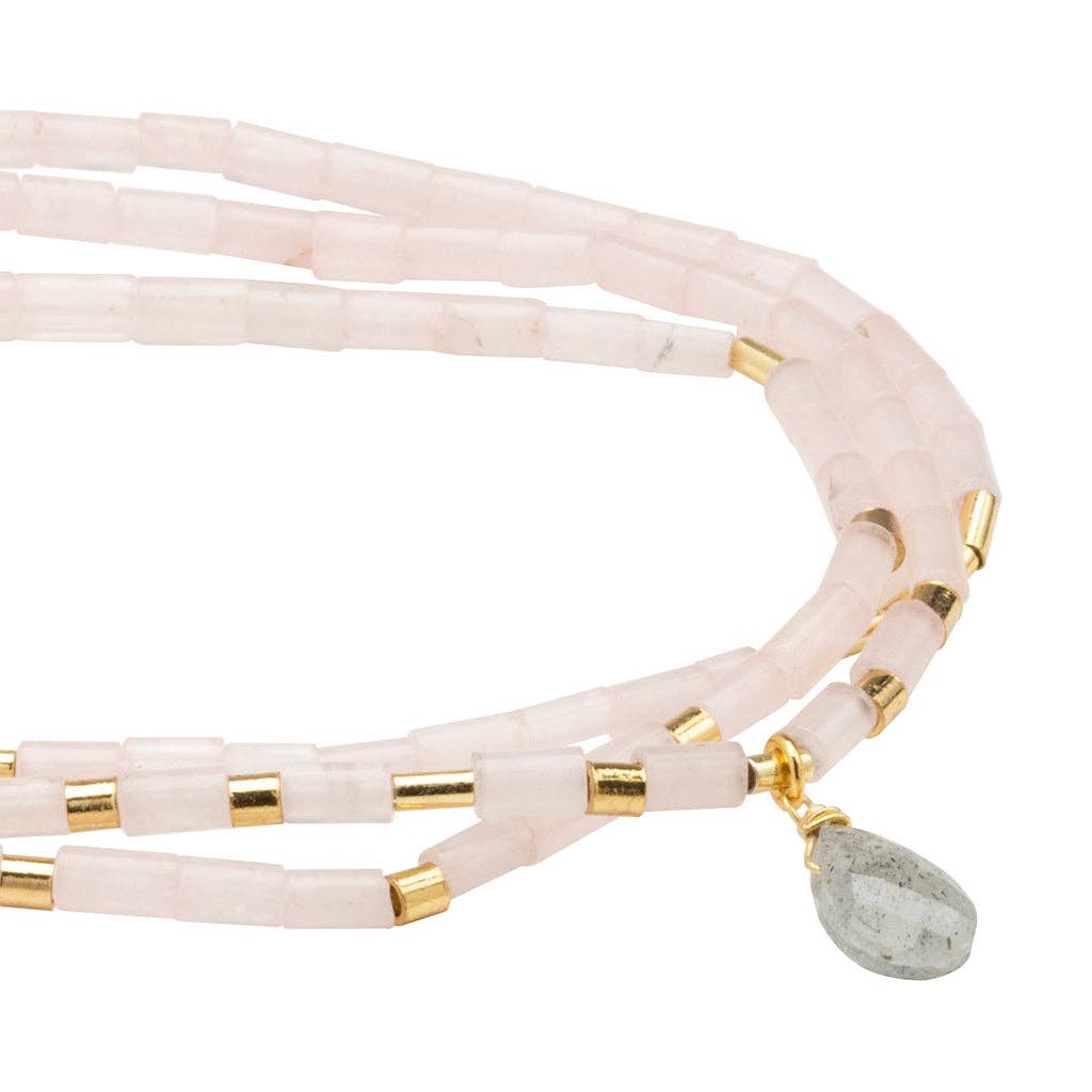 Pink multi-strand beaded bracelet with gold accents and a green stone charm on a white background