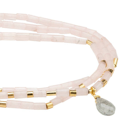 Pink multi-strand beaded bracelet with gold accents and a green stone charm on a white background