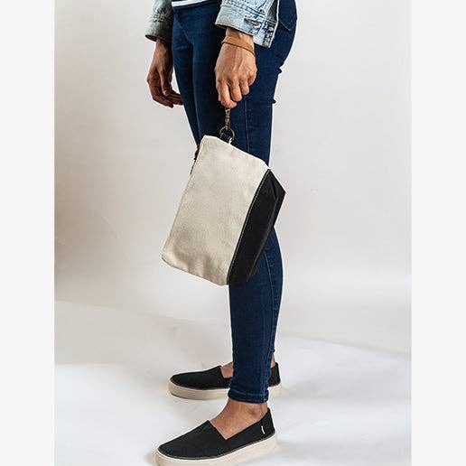 Person holding a beige and black clutch bag against a plain background