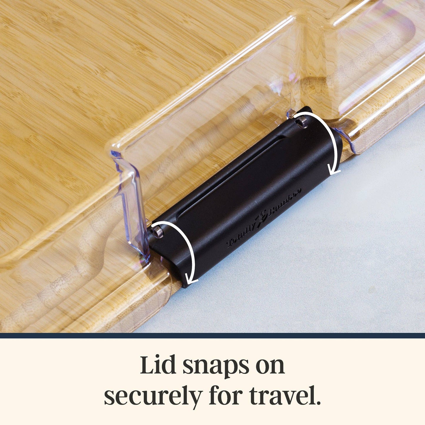 Black lid snap mechanism on the plastic lid of a wooden cutting board with text 'Lid snaps on securely for travel'.