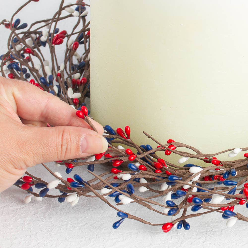 Decorative branch with red, blue, and white berries being held by a hand against a light background.