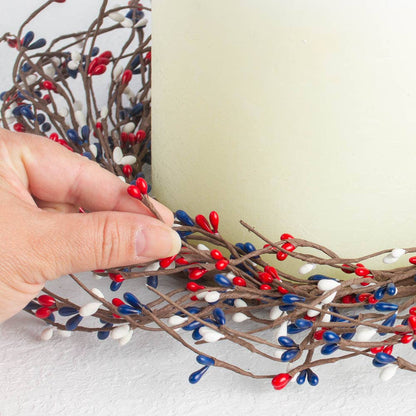 Decorative branch with red, blue, and white berries being held by a hand against a light background.