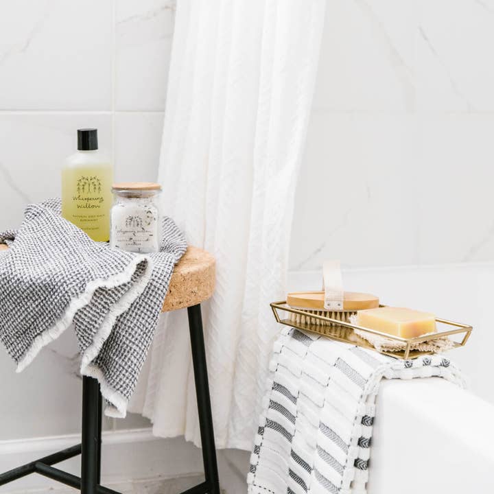 Bathroom setting with a stool, towel, and toiletries against a white curtain.
