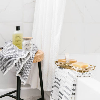 Bathroom setting with a stool, towel, and toiletries against a white curtain.