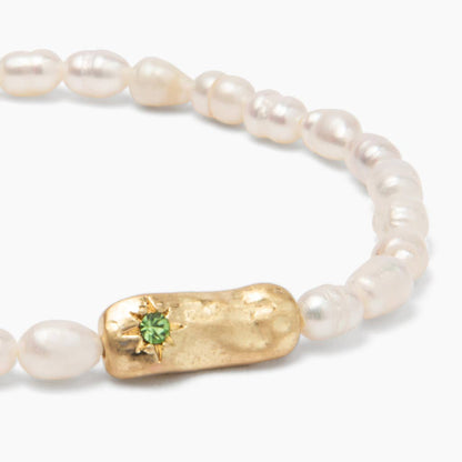 Detail of a pearl bracelet with gold bar and green gemstone on a white background. 
