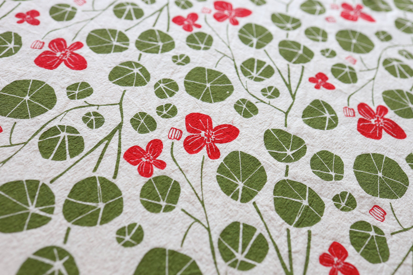 A close-up of a white tea towel featuring a repeating pattern of red flowers and green leaves.
