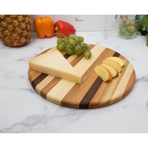 Round wooden cutting board with cheese, grapes, and bananas on a marble countertop.