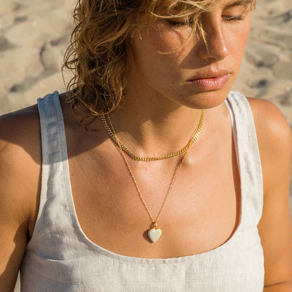 Woman wearing a gold necklace with a heart pendant on a beach