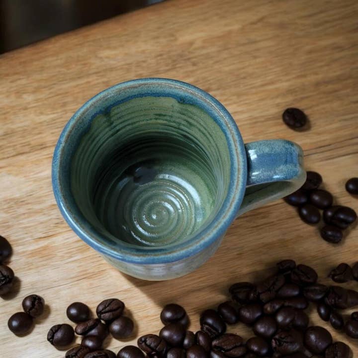 Green ceramic mug on a wooden surface with coffee beans around it