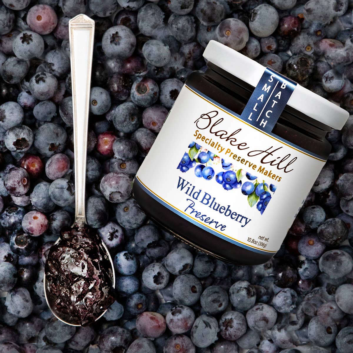 Jar of Blake Hill Wild Blueberry Preserve on a bed of blueberries with a spoonful of preserve.