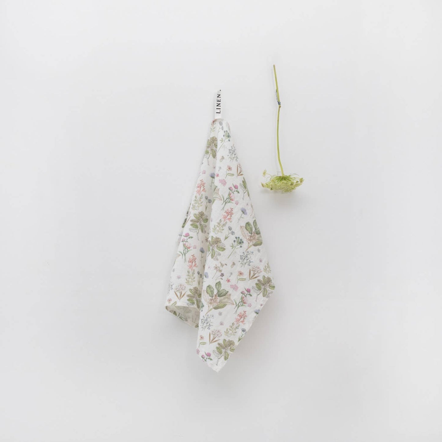 Floral-patterned towel hanging on a white wall with a Queen Anne's Lace stem