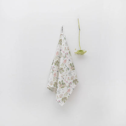Floral-patterned towel hanging on a white wall with a Queen Anne's Lace stem