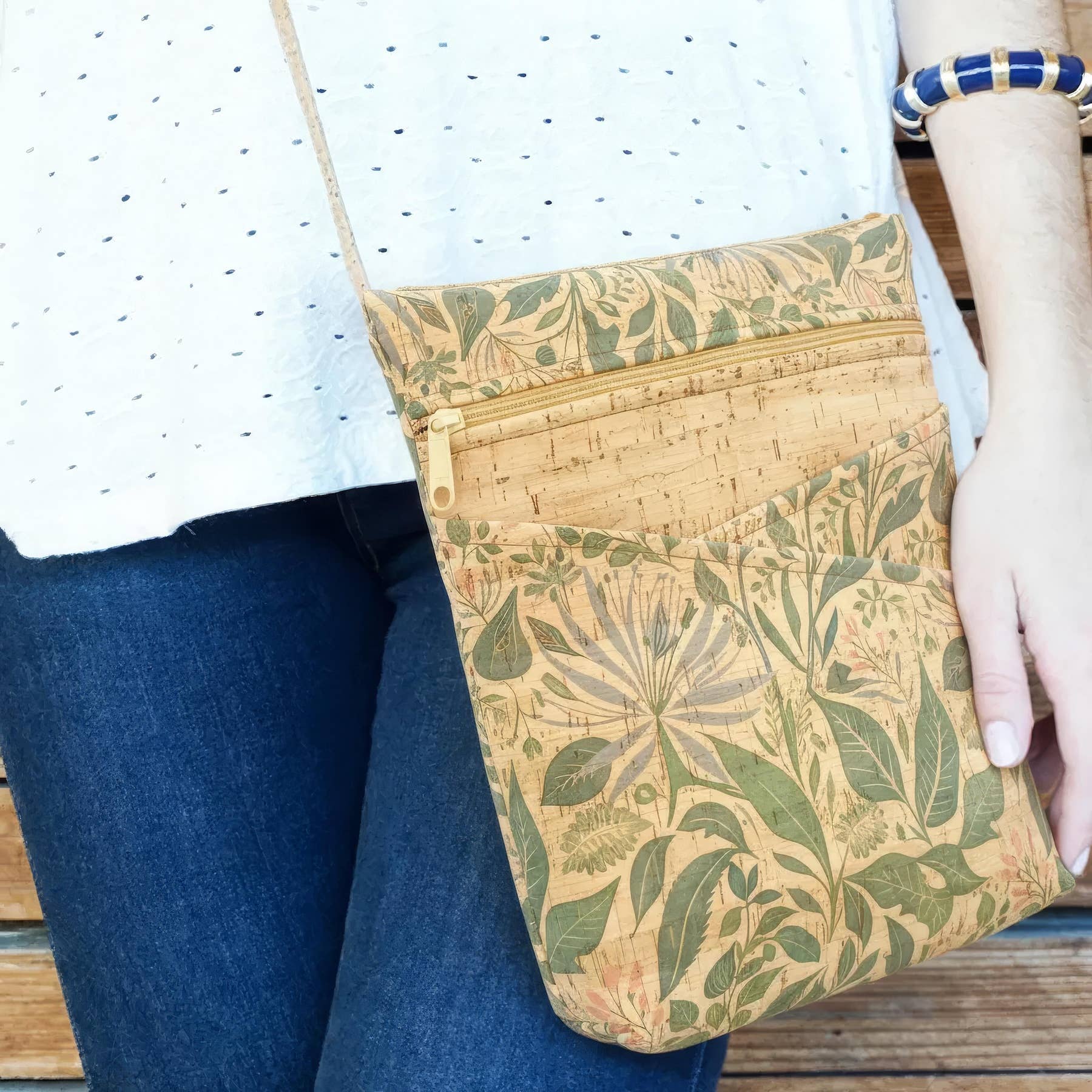 Person holding a floral-patterned cork bag and wearing a white shirt and blue jeans.