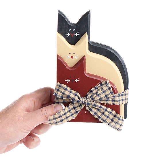 Cat-shaped decorative item with a checkered ribbon held by a hand on a white background