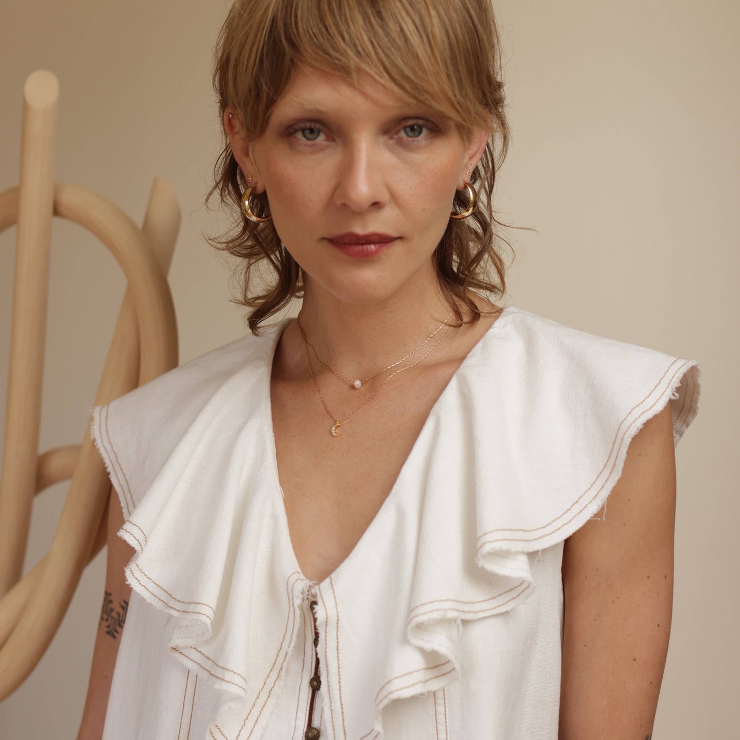 Woman wearing a white sleeveless top with ruffled details against a neutral background