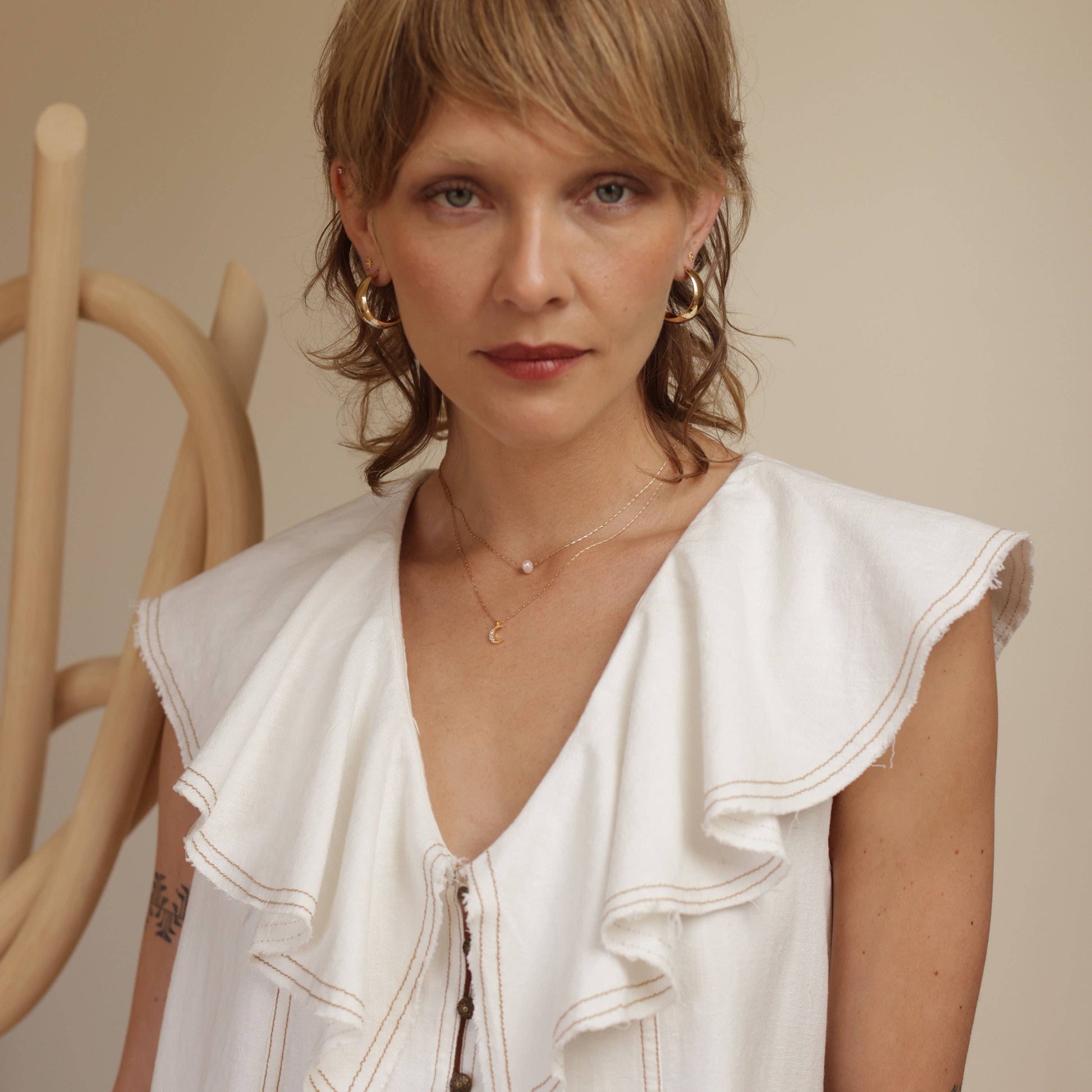 Woman wearing a white sleeveless top with ruffled details against a neutral background