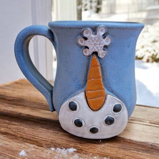 Blue ceramic mug with snowman design on a wooden surface