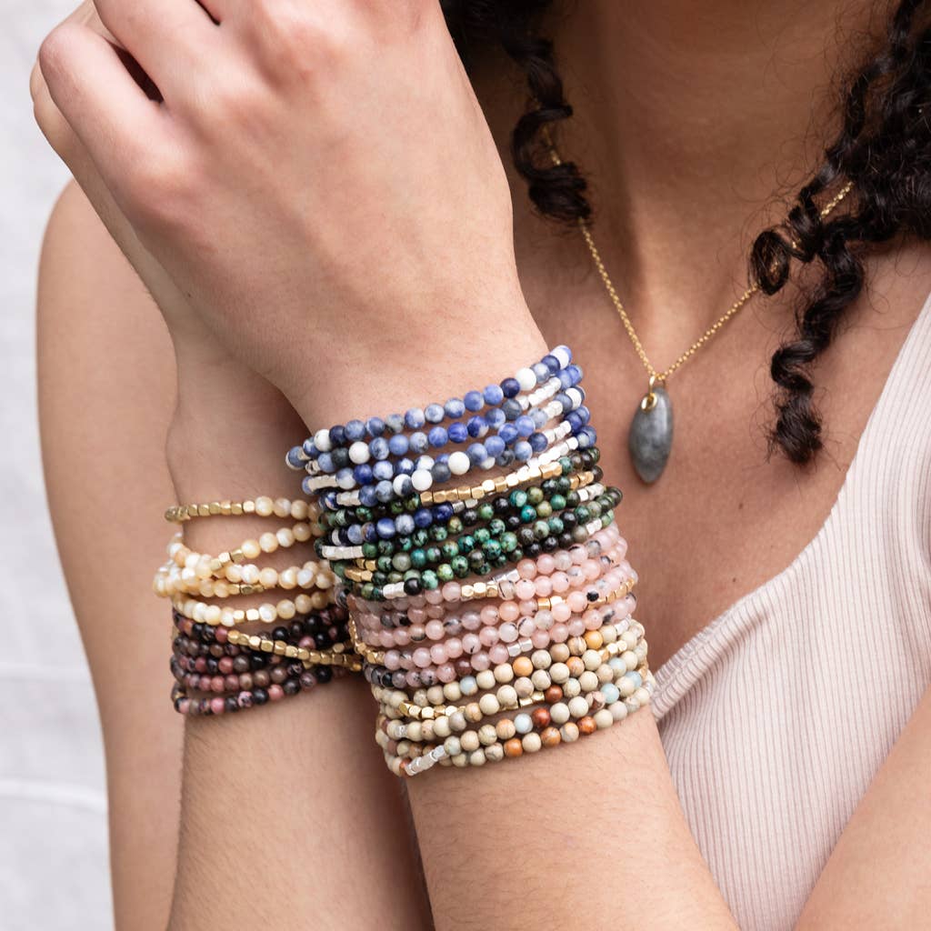 Close-up of a person's arm wearing multiple beaded bracelets on a plain background