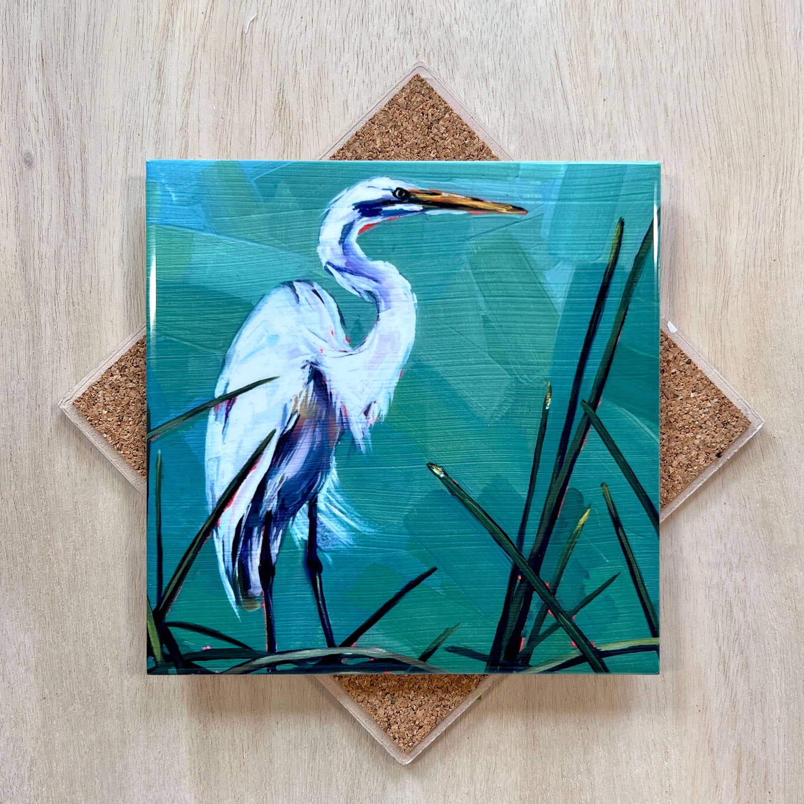 Coaster with a painting of a heron on a blue background, placed on a wooden surface.