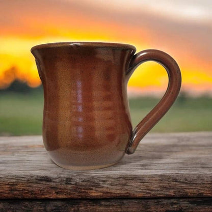 Brown ceramic mug on a wooden surface with a sunset background
