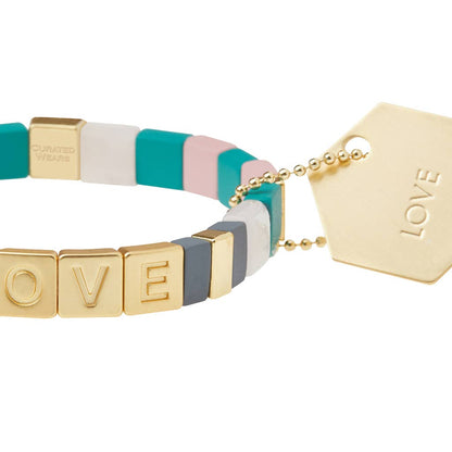 Bracelet with colorful band and gold 'LOVE' tag on a white background
