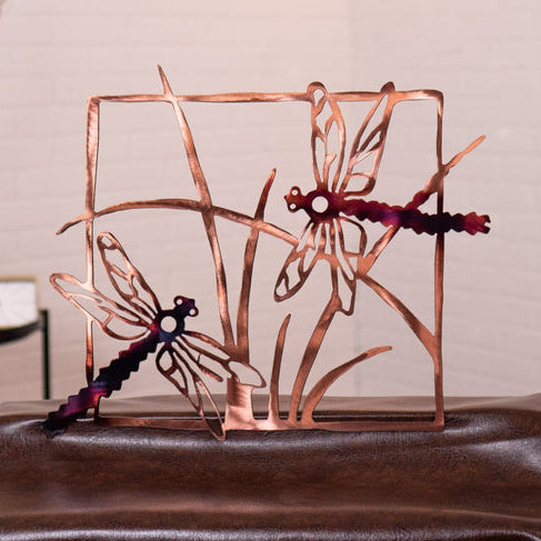 Copper dragonfly sculpture on a reflective surface with a neutral background