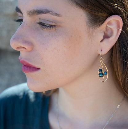 Close-up of a woman wearing a gold earring with green gemstones.