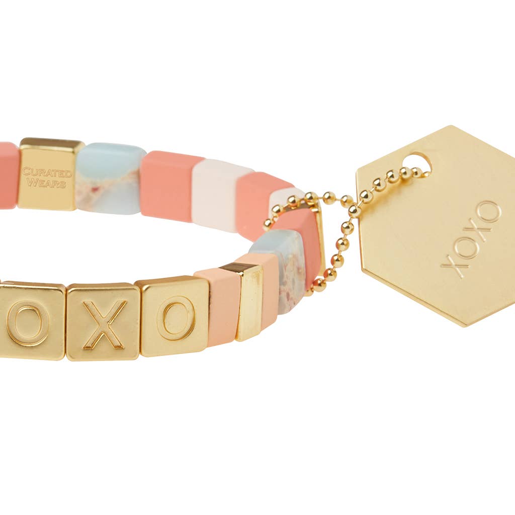 Bracelet with gold 'XO' beads and a hexagonal tag on a white background