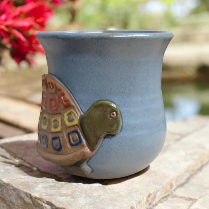 Ceramic mug with a decorative turtle on a stone surface with blurred natural background