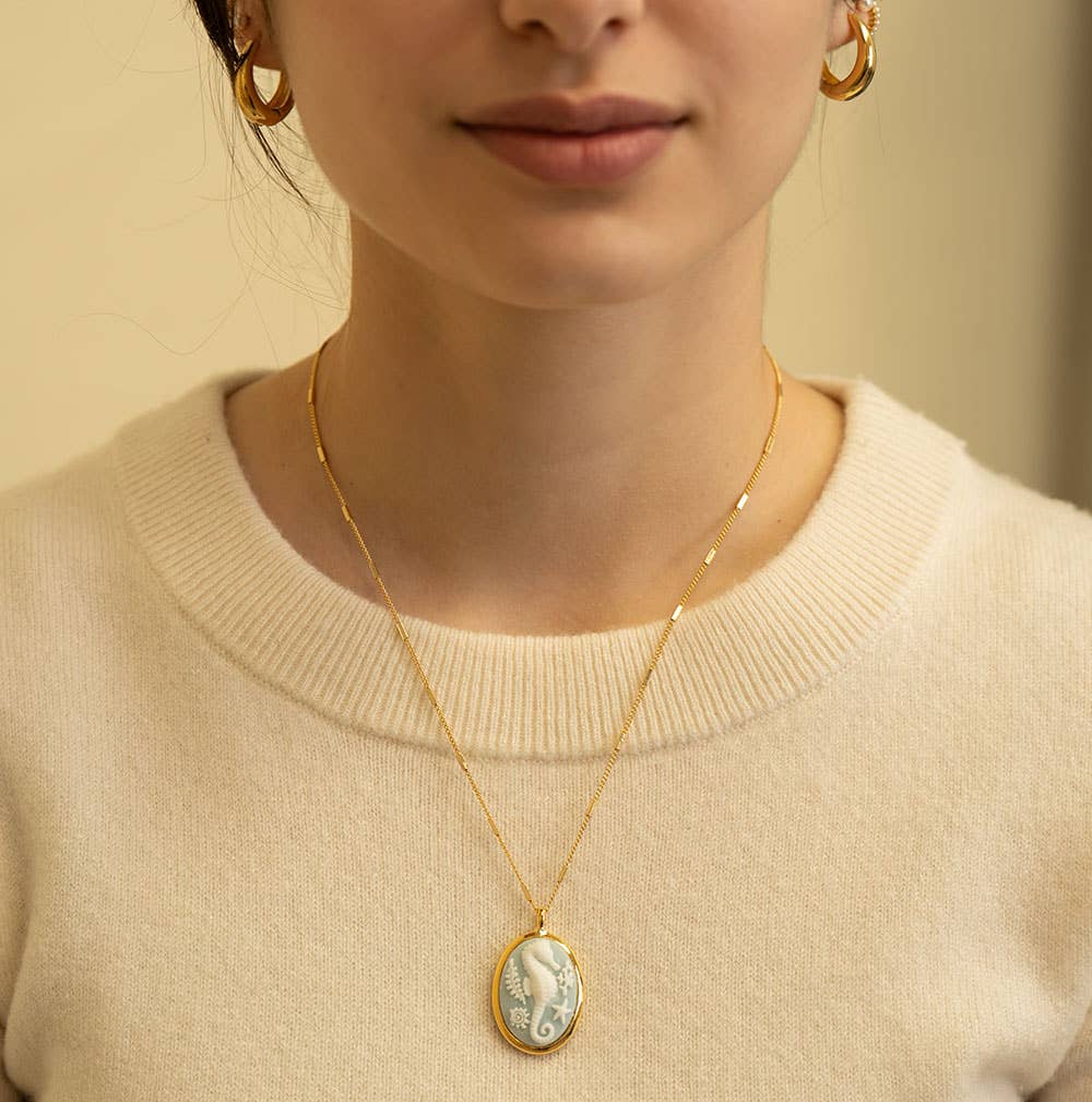 Person wearing a gold necklace with a pendant against a neutral background