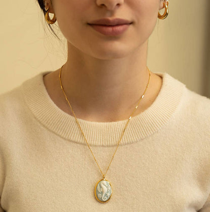 Person wearing a gold necklace with a pendant against a neutral background