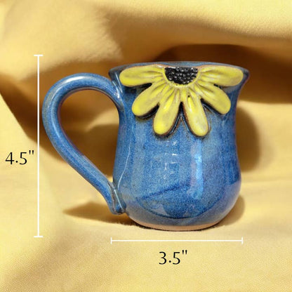 Blue ceramic mug with yellow black eyed Susan design on a yellow fabric background