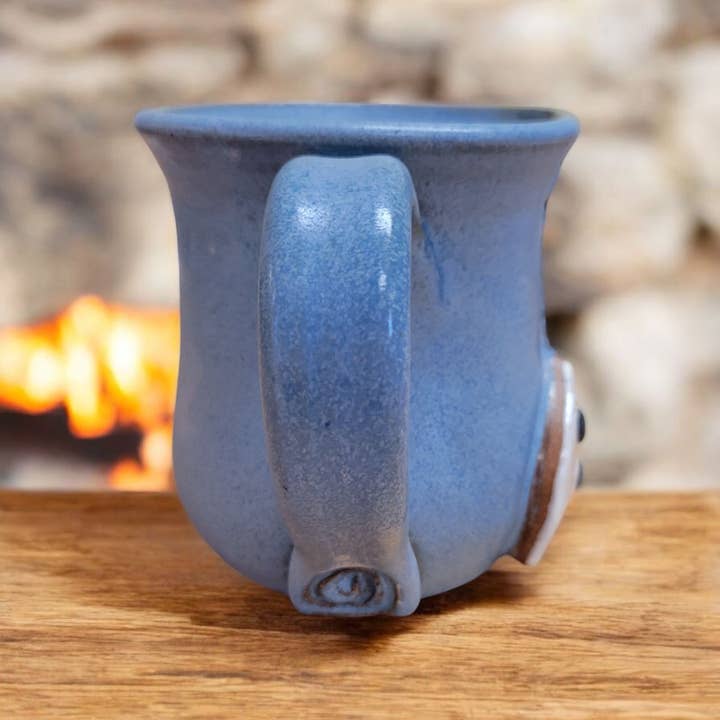 Blue ceramic mug on a wooden surface with a blurred background of fire and stones.