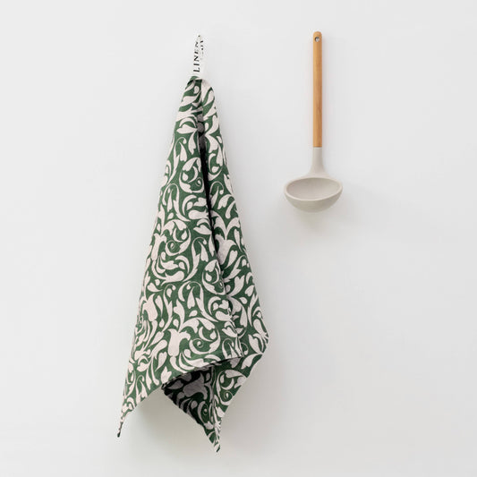 Green patterned towel hanging on a white wall with a wooden spoon.