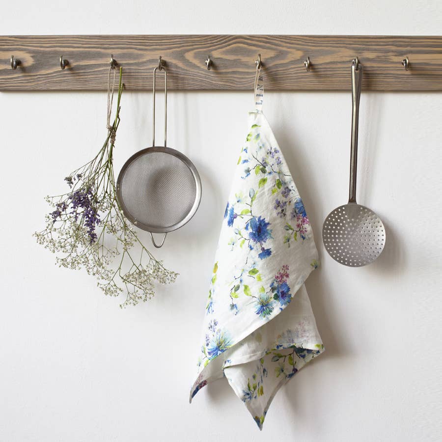 Kitchen utensils and a floral towel hanging on a wooden rack against a white wall.