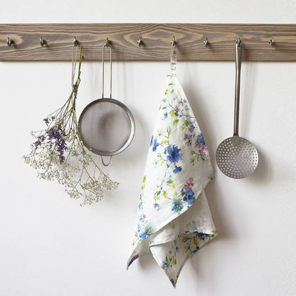 Kitchen utensils and a floral towel hanging on a wooden rack against a white wall.