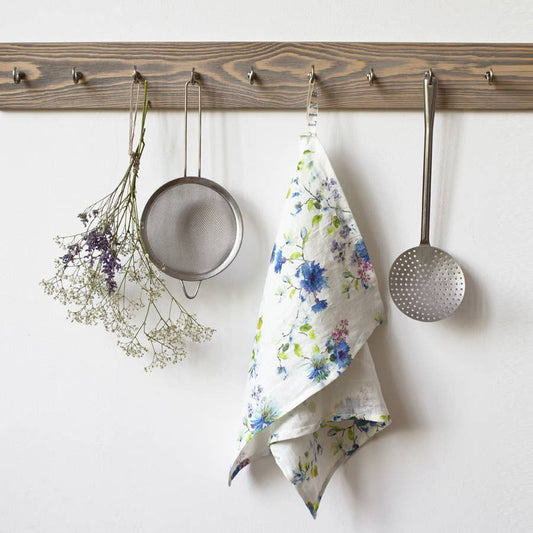 Kitchen utensils and a floral towel hanging on a wooden rack against a white wall.
