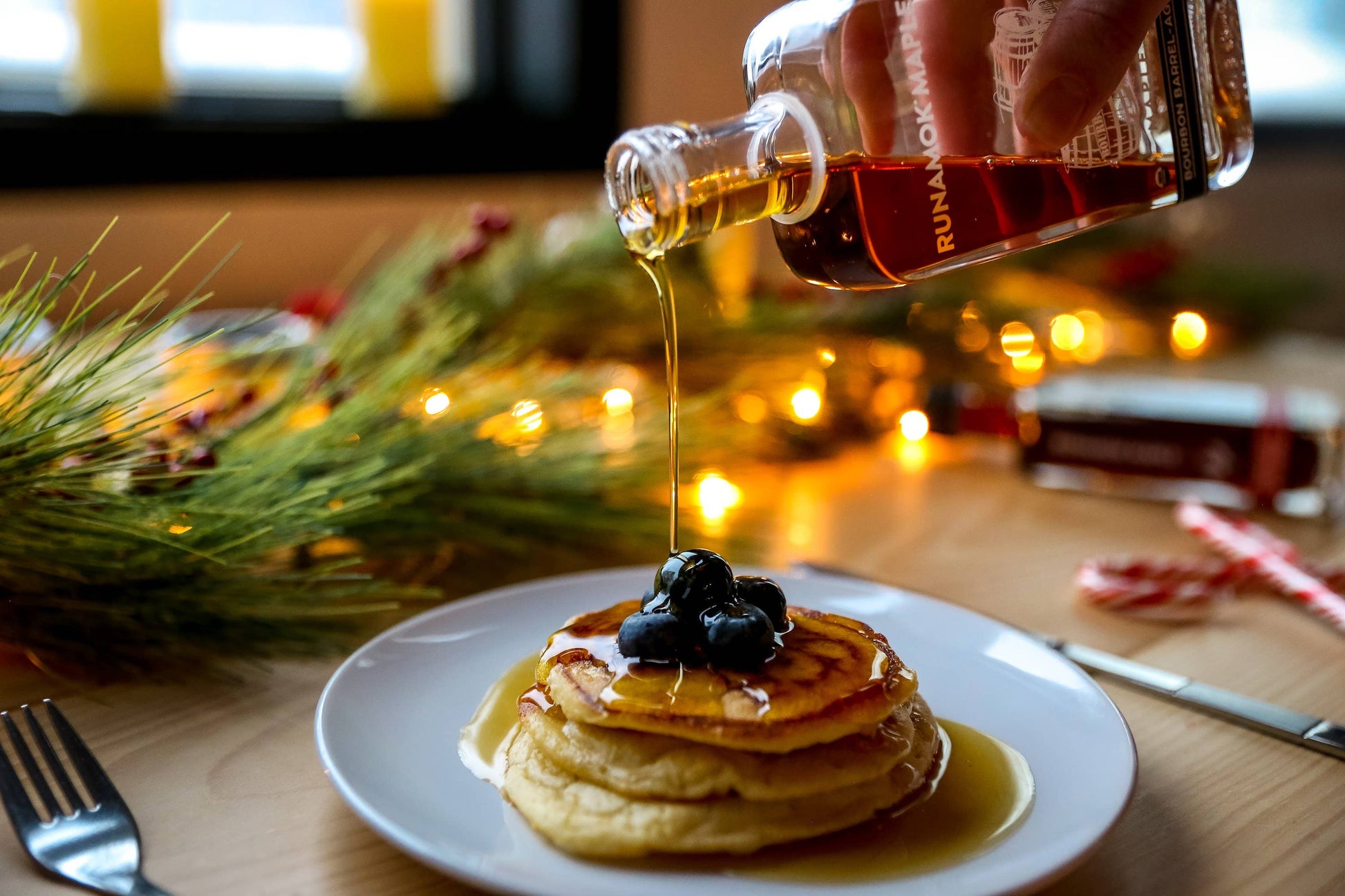 Person pouring syrup over pancakes with blueberries on a festive background