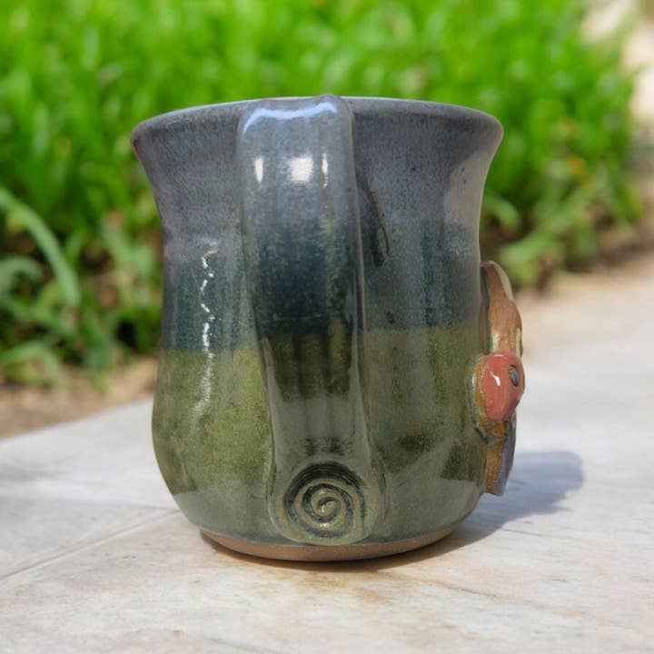 Ceramic mug with green and blue glaze on a wooden surface with a blurred natural background