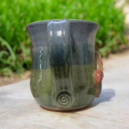 Ceramic mug with green and blue glaze on a wooden surface with a blurred natural background