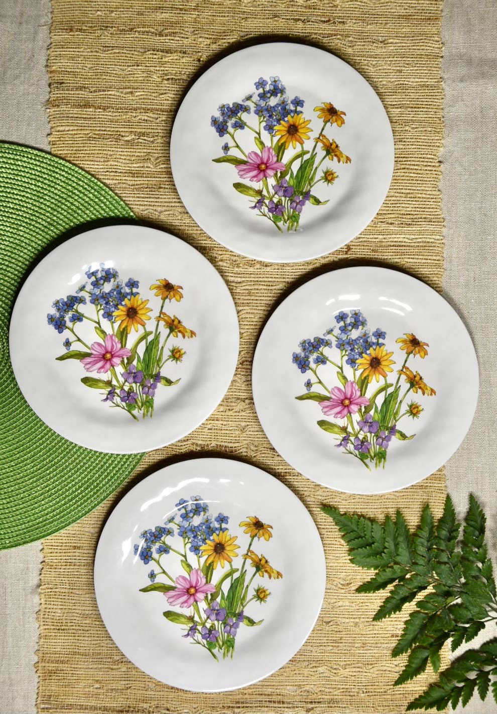 Four white plates with floral designs on a woven mat.