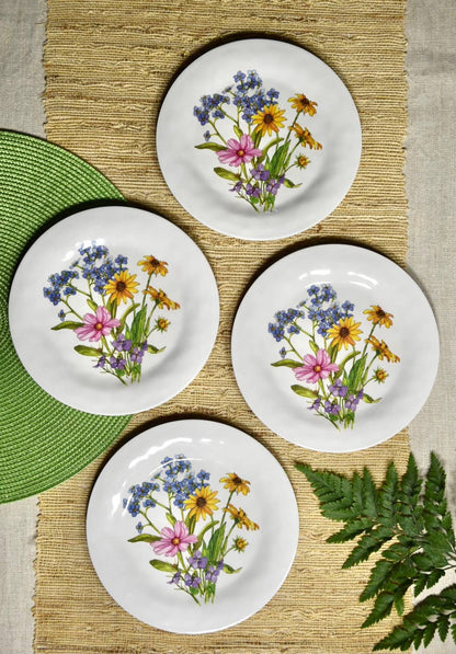 Four white plates with floral designs on a woven mat.