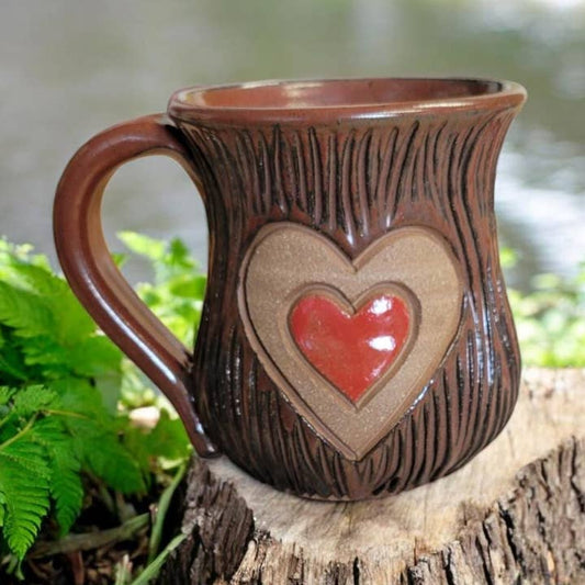 Ceramic mug with heart design on a wooden stump with greenery in the background